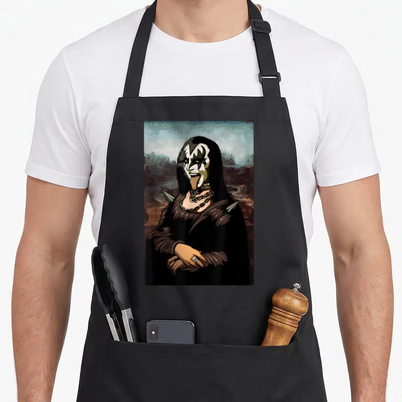 Rock funny halloween aprons - Portrait of Gene Simmons with demon makeup, tongue out, spikes, chains, and skull ring — shown on a black cotton canvas apron against a white background