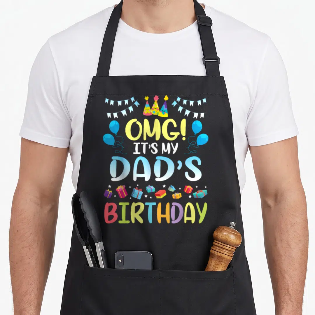 Omg daddy aprons - Stacked text OMG It's My Dad's Birthday surrounded by cartoon party hats, blue balloons — shown on a black cotton canvas apron against a white background