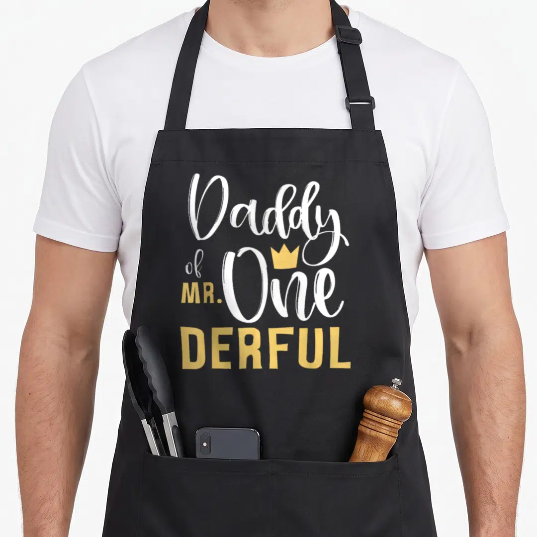 Onederful daddy apron - Daddy of MR One Derful text with small yellow crown above the word One — shown on a black cotton canvas apron against a white background