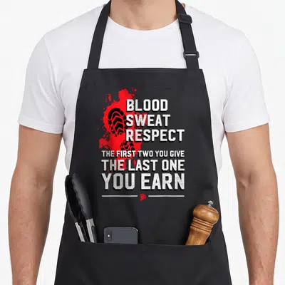 Sweat respect blood apron - Distressed white text over red splatter, black shoe print, and small red spartan helmet — shown on a black cotton canvas apron against a white background