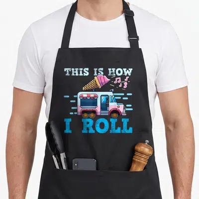 Truck ice cream apron - Cartoon ice cream truck with giant cone and text THIS IS HOW I ROLL in blue pink white and tan — shown on a black cotton canvas apron against a white background