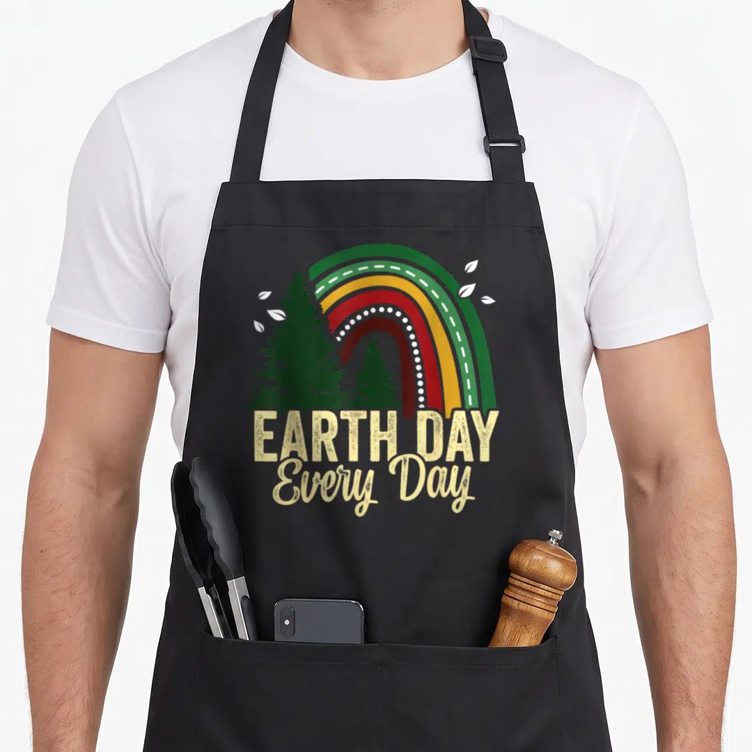 Everyday animal apron - Rainbow over three pine trees with white leaves and EARTH DAY Every Day text — shown on a black cotton canvas apron against a white background