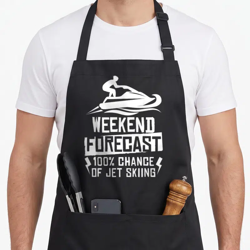 Weekend jet apron - White jet skier silhouette above WEEKEND FORECAST 100% CHANCE OF JET SKIING text with lightning — shown on a black cotton canvas apron against a white background