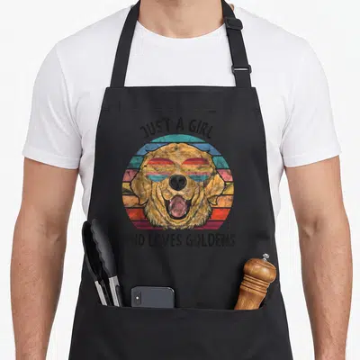 Dog golden retriever apron - Golden retriever wearing sunglasses over retro sunset circle with text Just a Girl Who — shown on a black cotton canvas apron against a white background