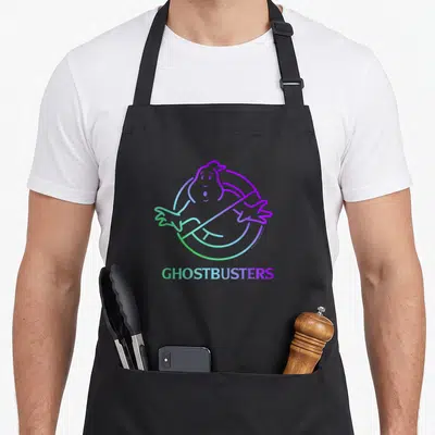 Ombre ghost apron - Cartoon ghost inside prohibition circle with GHOSTBUSTERS text in green blue purple gradient — shown on a black cotton canvas apron against a white background