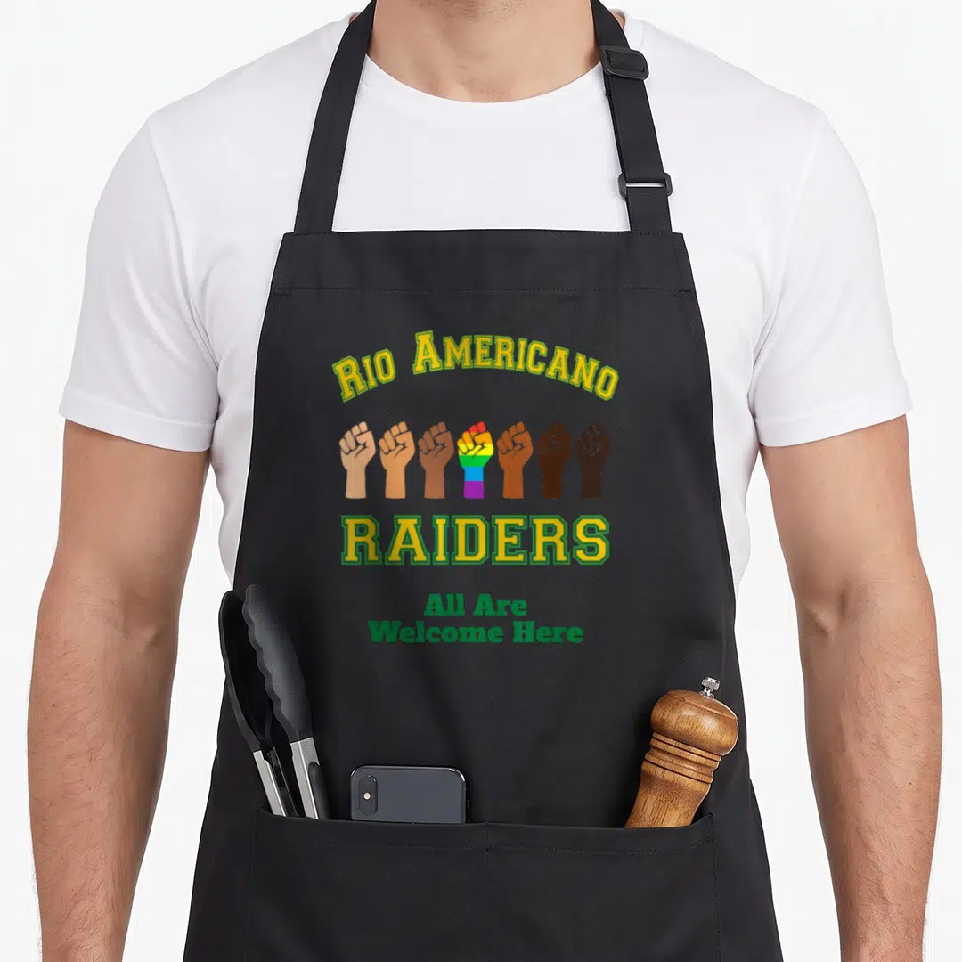 Rio americana apron - Seven raised fists including one rainbow fist below arched Rio Americano Raiders text — shown on a black cotton canvas apron against a white background