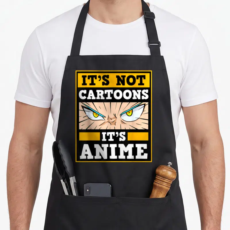 Anime cartoon apron - Angry anime eyes with It's Not Cartoons It's Anime text in yellow black frame — shown on a black cotton canvas apron against a white background