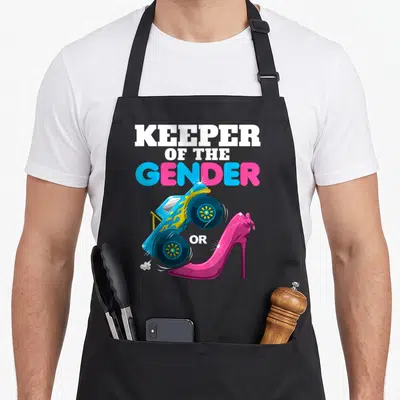 Heel wheel apron - Stacked text KEEPER OF THE GENDER OR above blue monster truck and pink high heel shoe — shown on a black cotton canvas apron against a white background