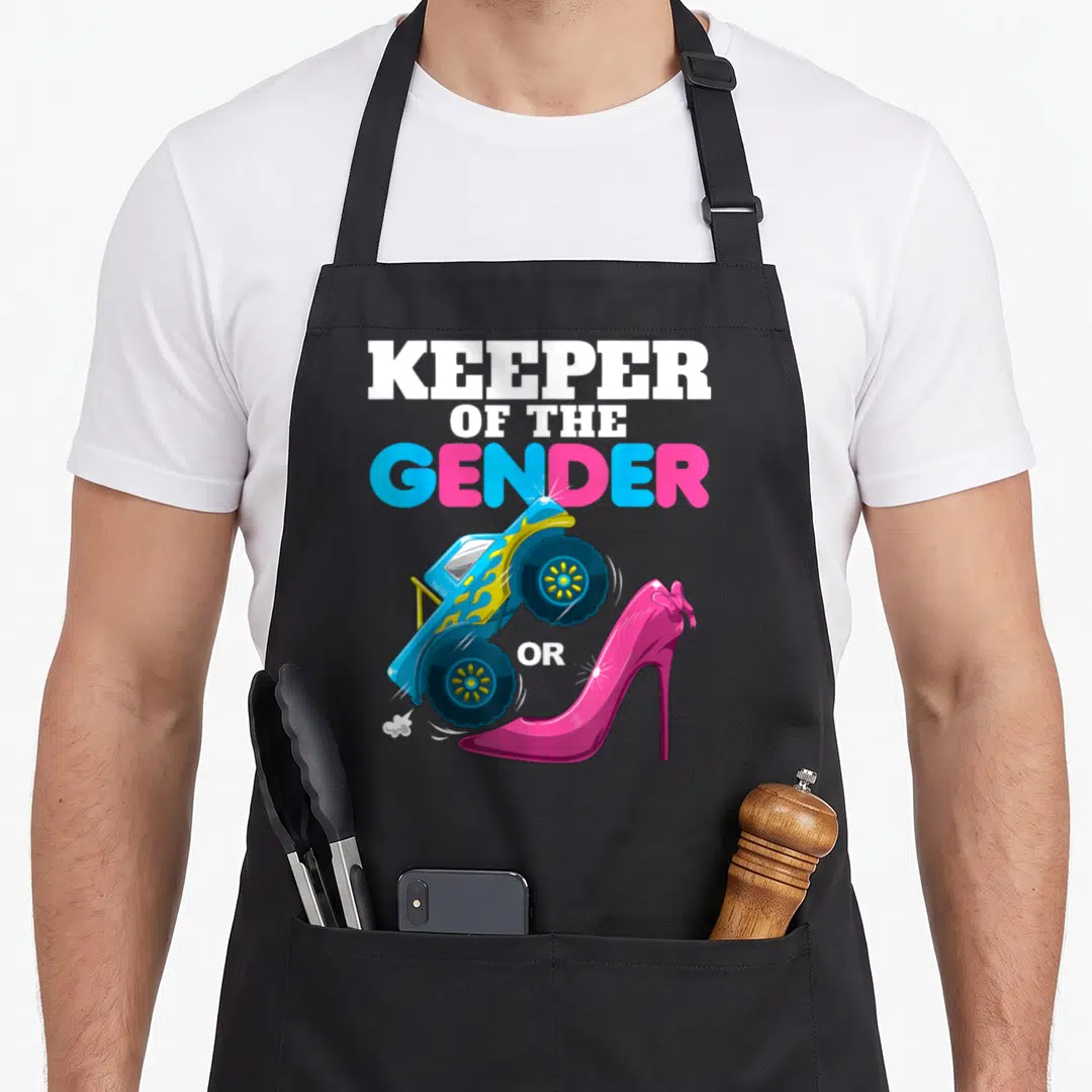 Heel wheel apron - Stacked text KEEPER OF THE GENDER OR above blue monster truck and pink high heel shoe — shown on a black cotton canvas apron against a white background