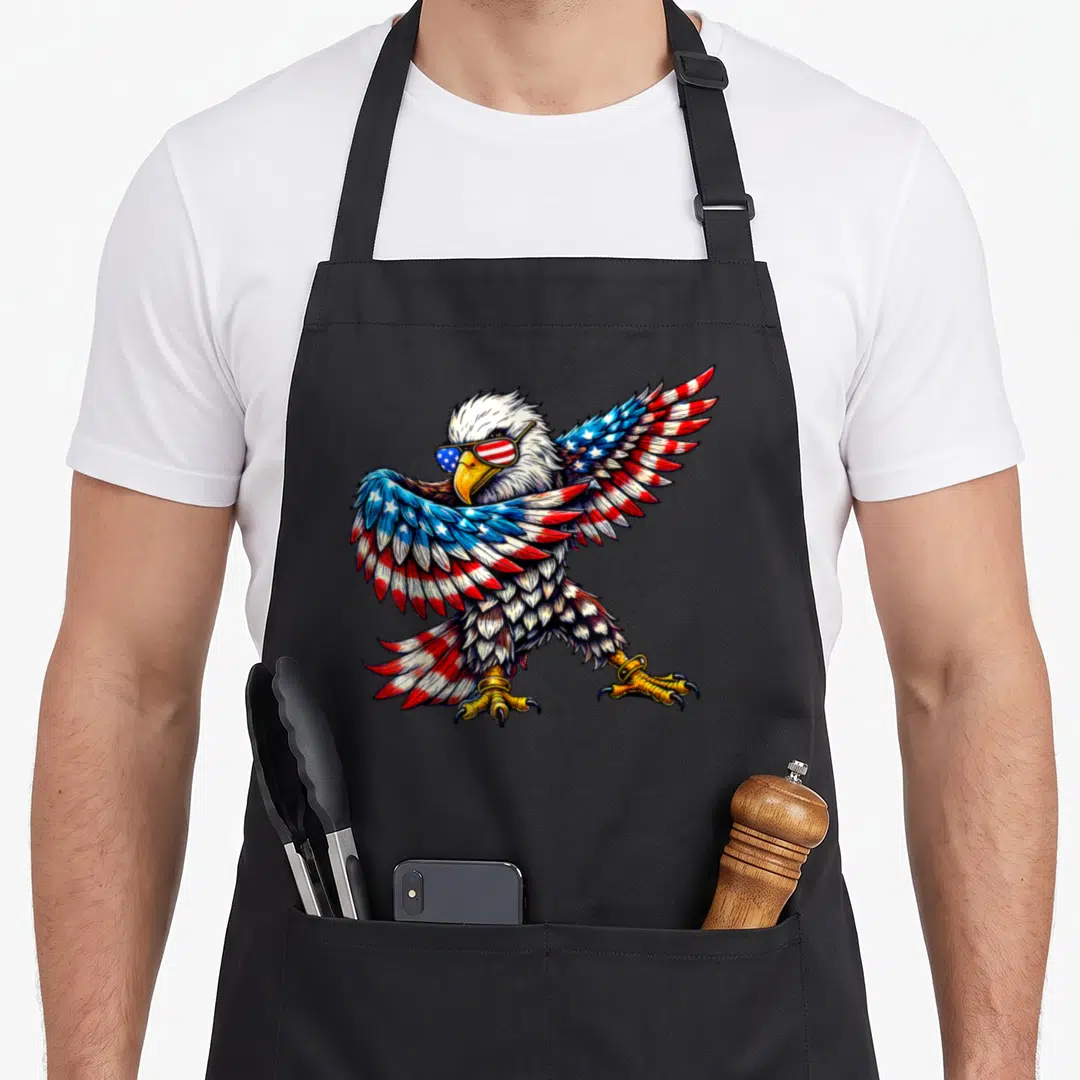 Eagle patriotic 4th of july apron - Bald eagle wearing sunglasses with red white and blue flag pattern wings — shown on a black cotton canvas apron against a white background