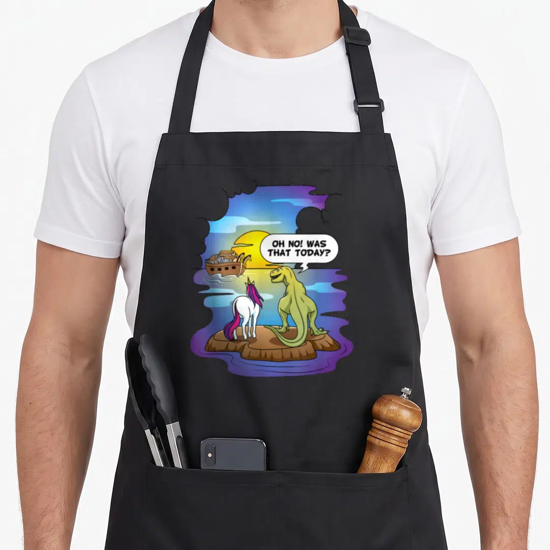 Bibble christian apron - Cartoon dinosaur and unicorn watching Noah's Ark sail away under a sunset — shown on a black cotton canvas apron against a white background