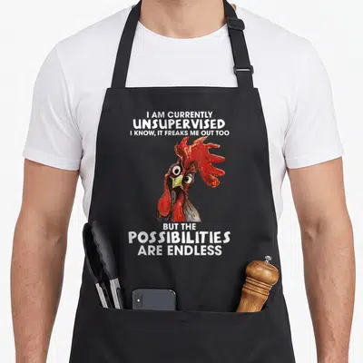 Unsupervised freak apron - Rooster head with white text reading I am currently unsupervised on grey background — shown on a black cotton canvas apron against a white background