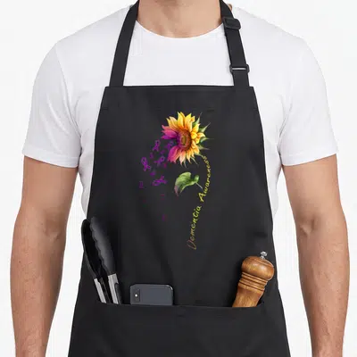 Dementia sunflower apron - Watercolor sunflower with purple ribbons and curved yellow text on grey background — shown on a black cotton canvas apron against a white background