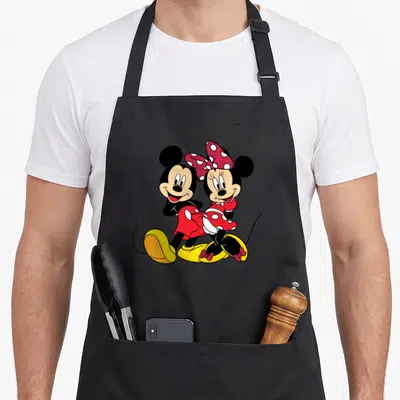 Funny mouse apron - Mickey and Minnie Mouse standing close together in a cartoon style wearing red and yellow outfits — shown on a black cotton canvas apron against a white background