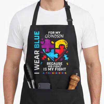 Grandpa grandma apron - Multi-colored puzzle heart with vertical text I WEAR BLUE and Autism Awareness slogan — shown on a black cotton canvas apron against a white background