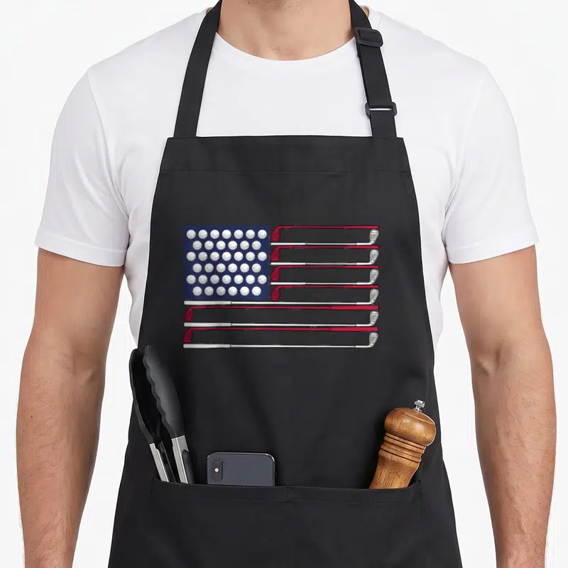 Golf 4th of july apron - American flag made of white golf balls and red white clubs on blue background — shown on a black cotton canvas apron against a white background