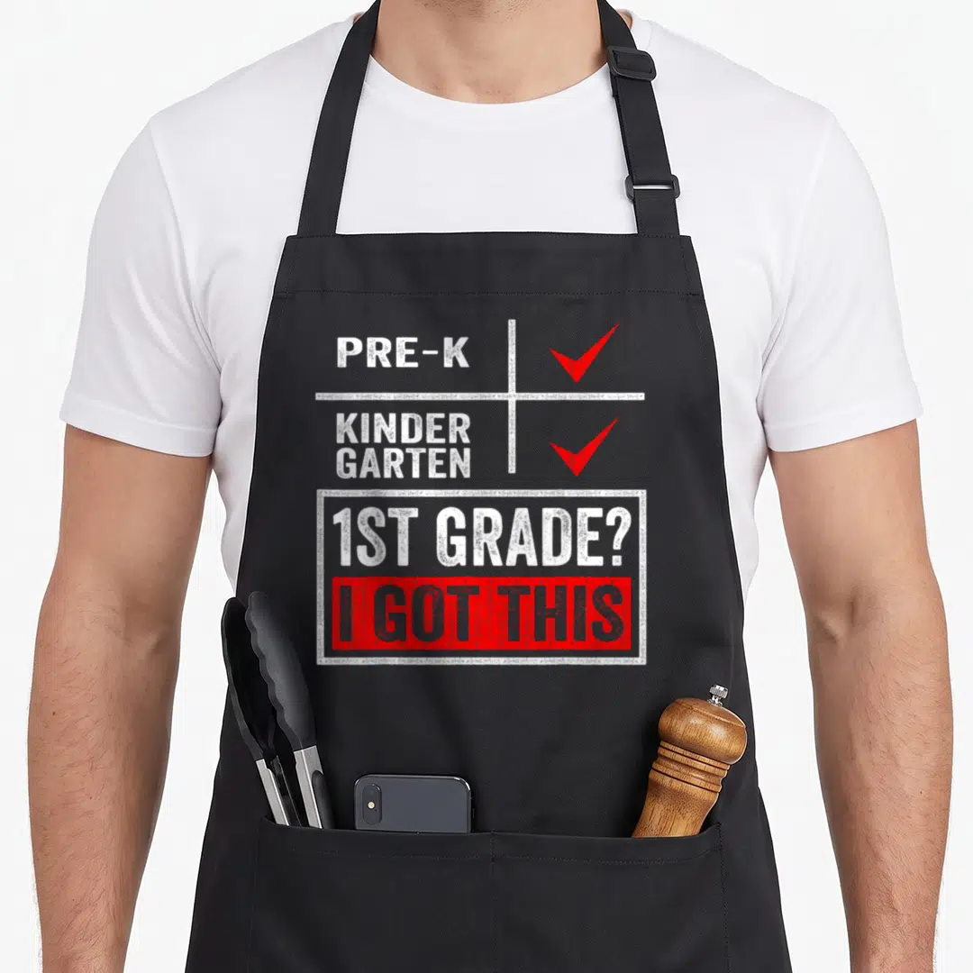 Grade school apron - Distressed white and red checklist with check marks for Pre-K and Kindergarten, 1st Grade — shown on a black cotton canvas apron against a white background