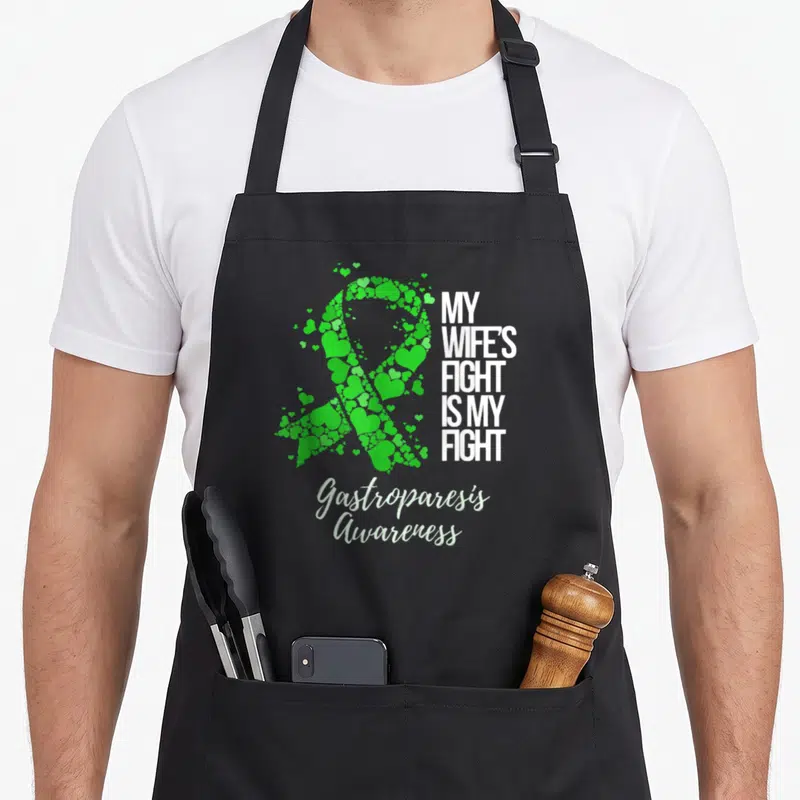 Gastroparesis wife apron - Green scattered hearts forming a ribbon next to white block text and script lettering — shown on a black cotton canvas apron against a white background