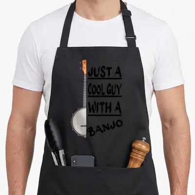 Bluegrass player banjo apron - Vertical banjo with orange headstock next to stacked black text JUST A COOL GUY — shown on a black cotton canvas apron against a white background