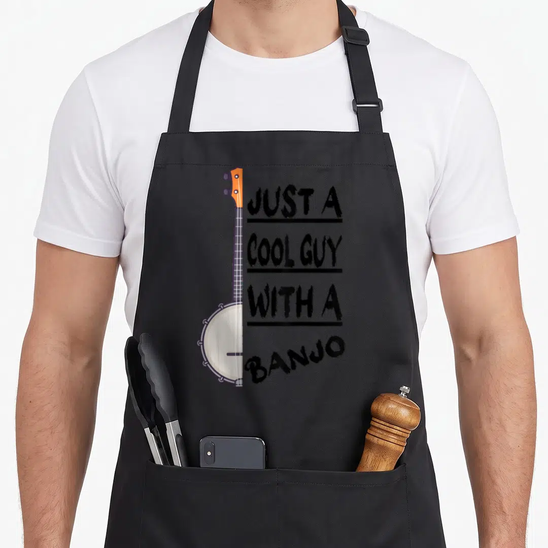 Bluegrass player banjo apron - Vertical banjo with orange headstock next to stacked black text JUST A COOL GUY — shown on a black cotton canvas apron against a white background