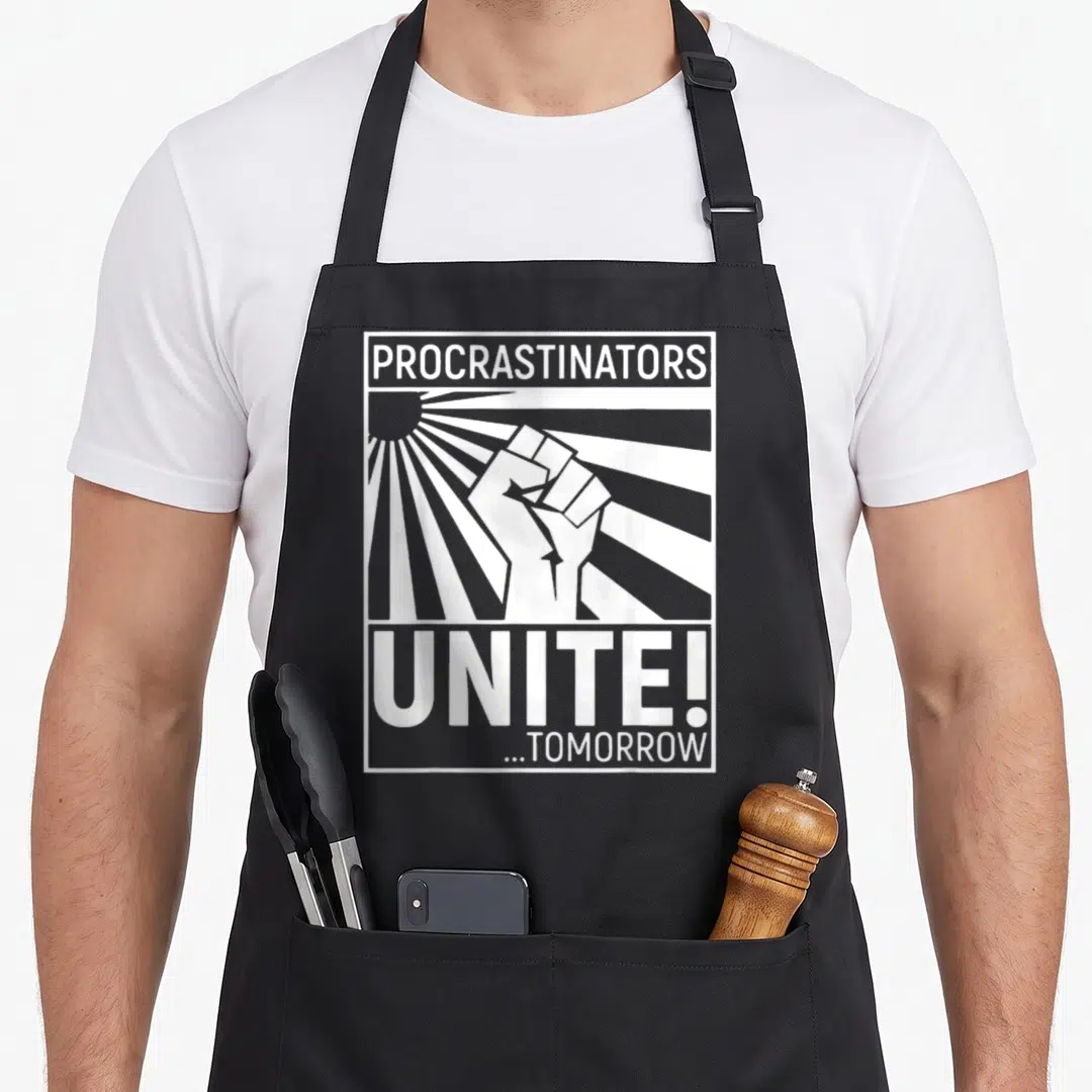 Funny unite procrastinator apron - Raised fist over sunburst with text PROCRASTINATORS UNITE ...TOMORROW in white — shown on a black cotton canvas apron against a white background