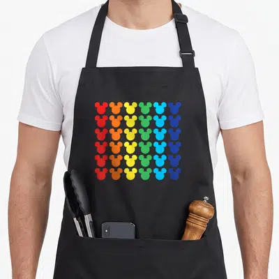 Icon rainbow apron - Grid of thirty-six mouse head silhouettes in red, orange, yellow, green, and blue columns — shown on a black cotton canvas apron against a white background