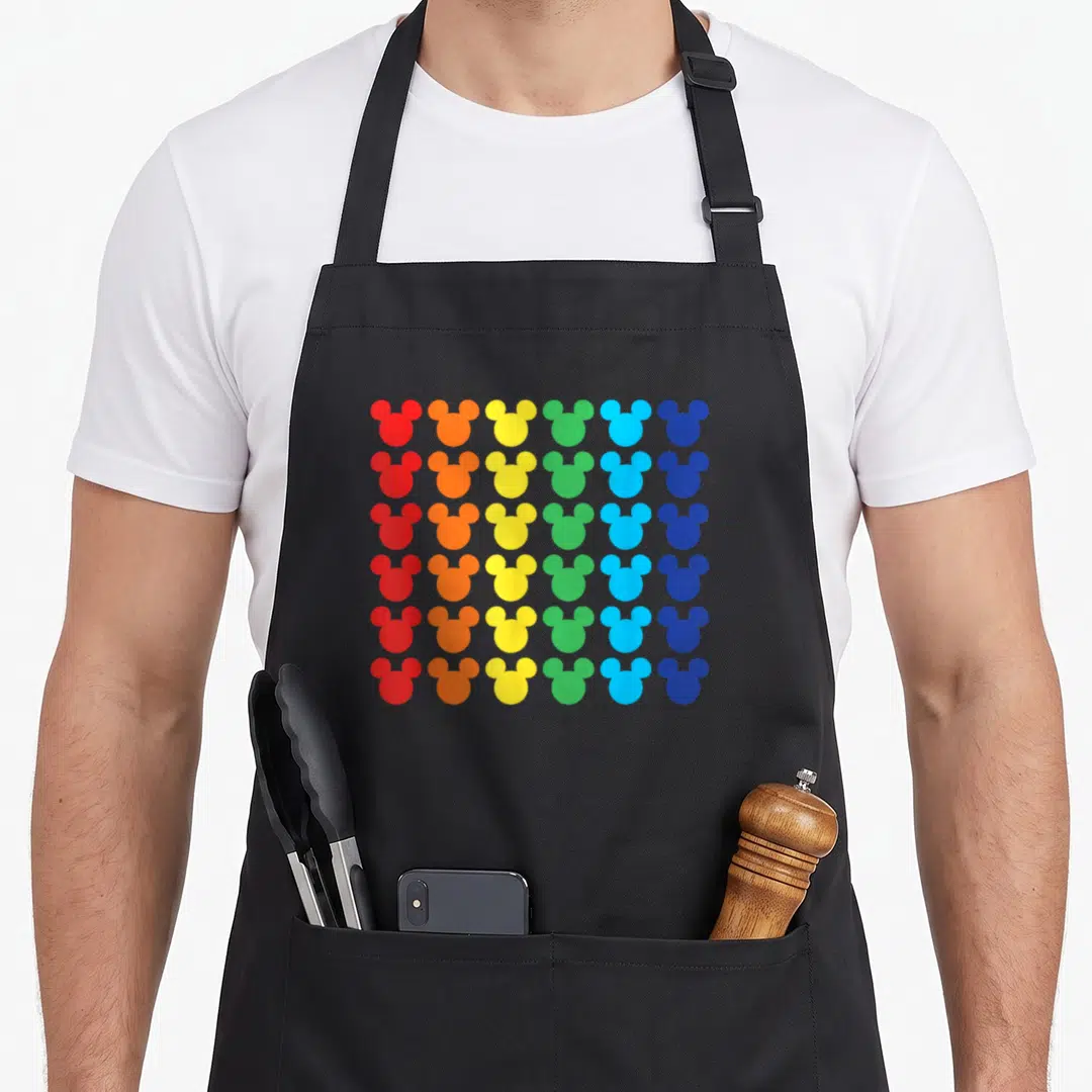 Icon rainbow apron - Grid of thirty-six mouse head silhouettes in red, orange, yellow, green, and blue columns — shown on a black cotton canvas apron against a white background