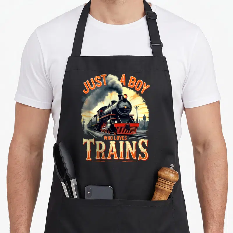 Vintage train steam locomotive apron - Retro steam locomotive illustration with orange JUST A BOY WHO LOVES TRAINS text — shown on a black cotton canvas apron against a white background
