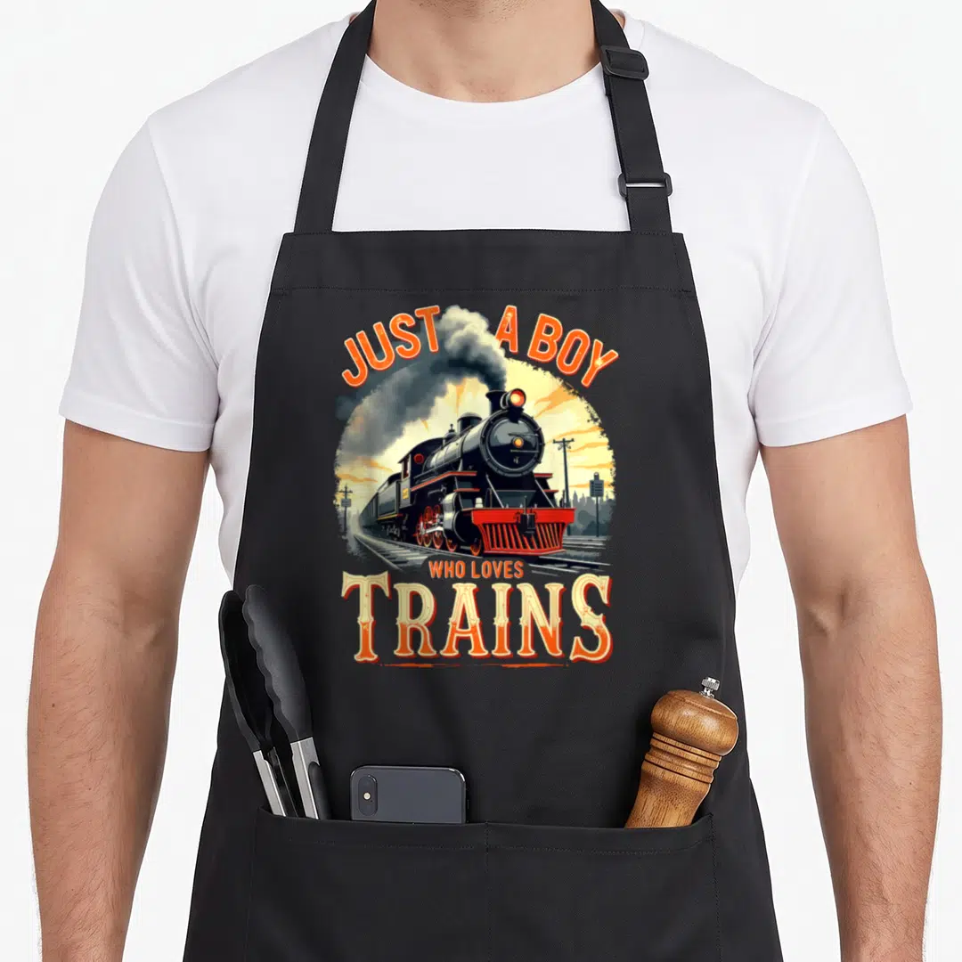 Vintage train steam locomotive apron - Retro steam locomotive illustration with orange JUST A BOY WHO LOVES TRAINS text — shown on a black cotton canvas apron against a white background