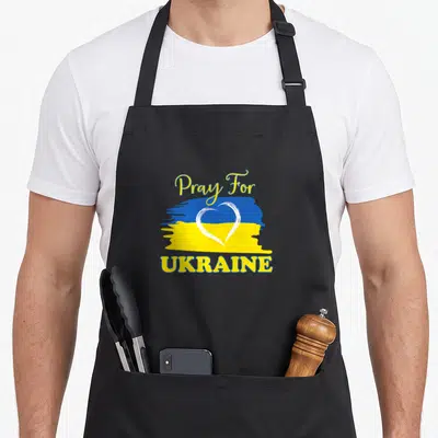 Pray ukrainian aprons - Blue yellow flag with white heart outline and Pray For UKRAINE text — shown on a black cotton canvas apron against a white background