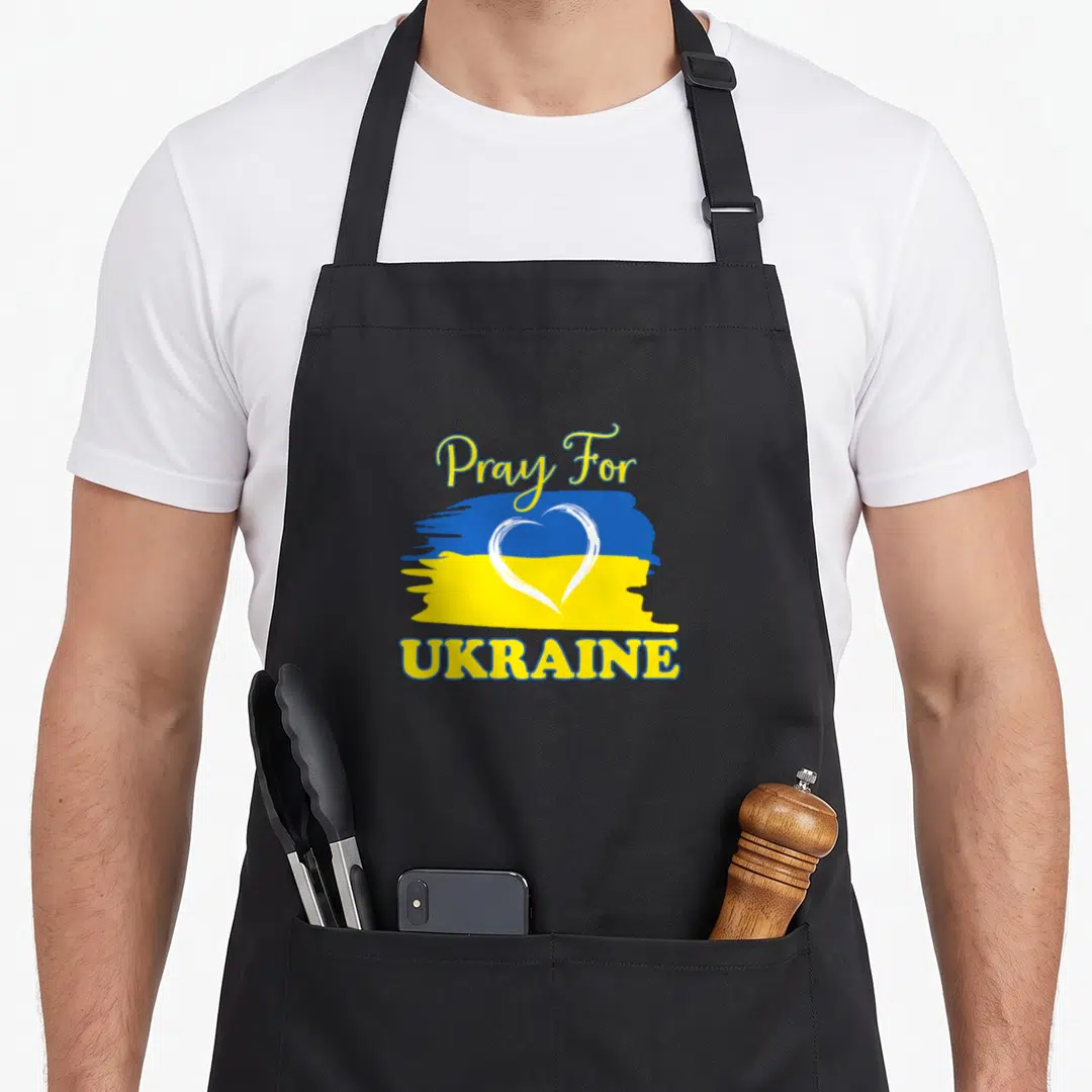 Pray ukrainian aprons - Blue yellow flag with white heart outline and Pray For UKRAINE text — shown on a black cotton canvas apron against a white background