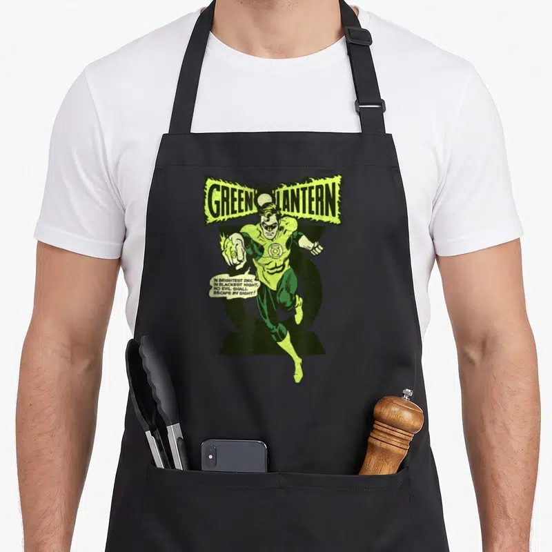 Lantern comedian apron - Green Lantern flying character with oath speech bubble in green yellow and black — shown on a black cotton canvas apron against a white background
