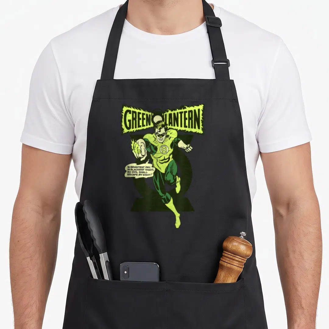 Lantern comedian apron - Green Lantern flying character with oath speech bubble in green yellow and black — shown on a black cotton canvas apron against a white background