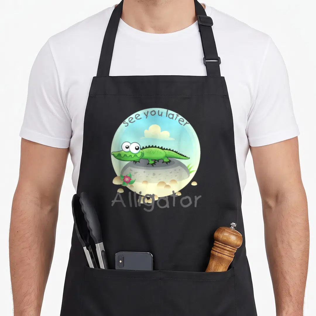 Alligator florida apron - Cartoon green alligator on grey rock inside blue circle with see you later text and pink — shown on a black cotton canvas apron against a white background