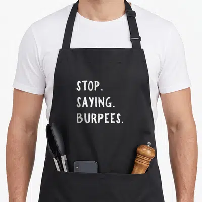 Stop personal apron - White stacked text reading STOP. SAYING. BURPEES. on a dark background — shown on a black cotton canvas apron against a white background