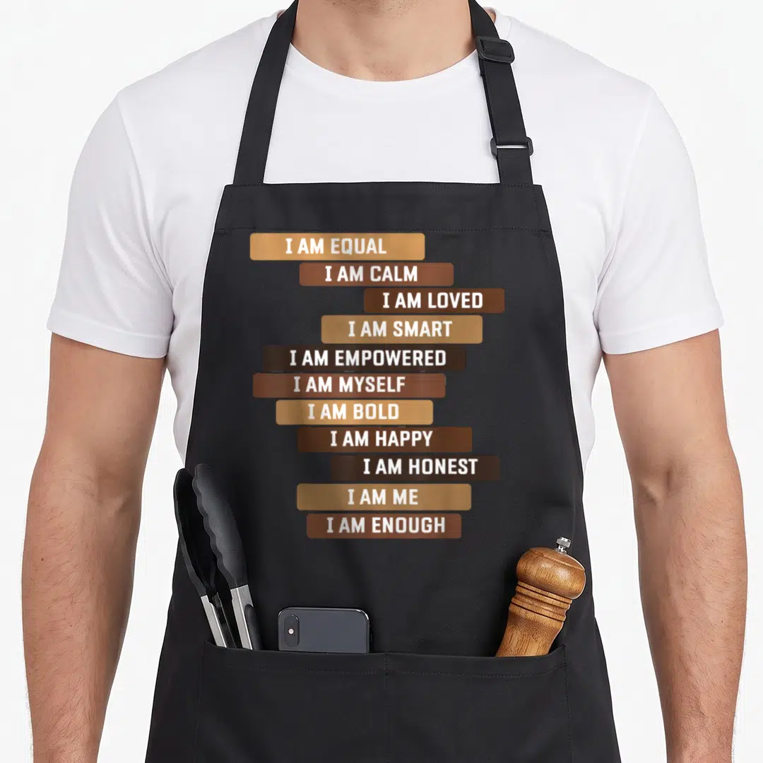 Melanin motivation apron - Stacked brown and tan bars with white I AM affirmation text — shown on a black cotton canvas apron against a white background