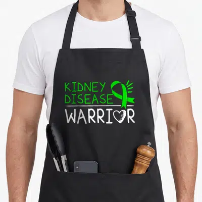 Ckd kidney disease awareness apron - Green Kidney Disease Warrior text with ribbon and heart O on black bib — shown on a black cotton canvas apron against a white background