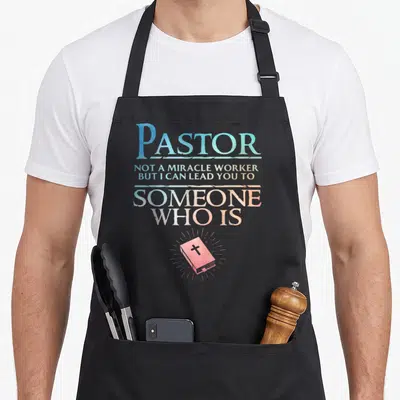 Appreciation clergy apron - Stacked pastel text reading Pastor Not A Miracle Worker above a glowing pink bible — shown on a black cotton canvas apron against a white background