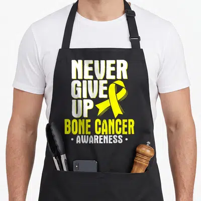 Ewing bone cancer awareness apron - Yellow ribbon overlapping white NEVER GIVE UP text with BONE CANCER AWARENESS below — shown on a black cotton canvas apron against a white background