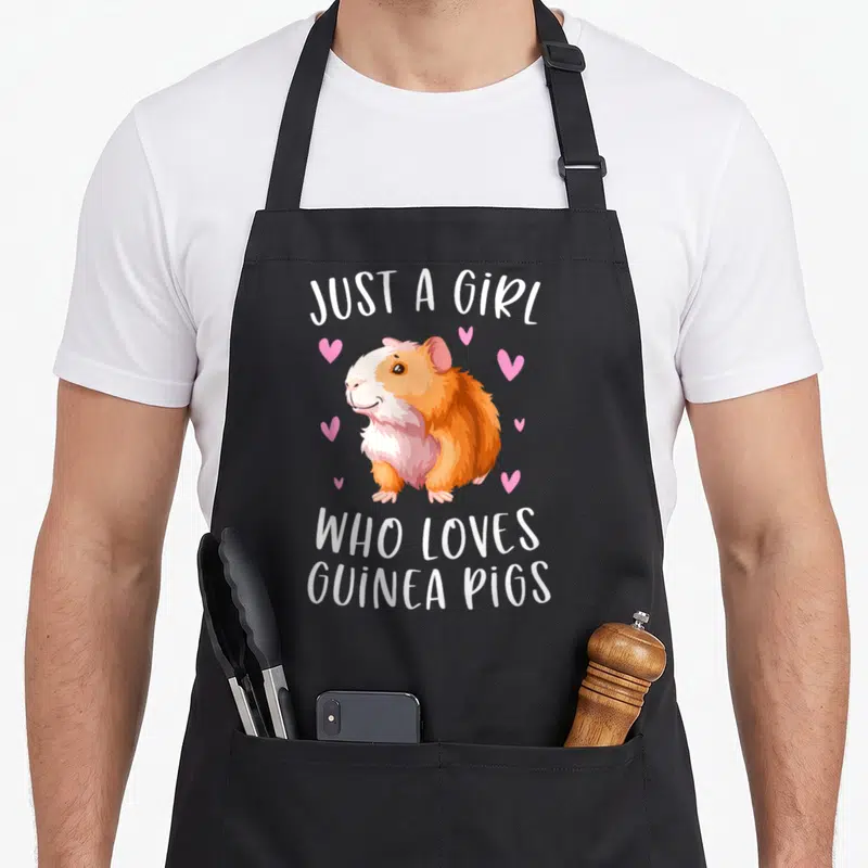 Cavy crazy guinea lady apron - Cartoon guinea pig in orange and white with pink hearts and text — shown on a black cotton canvas apron against a white background