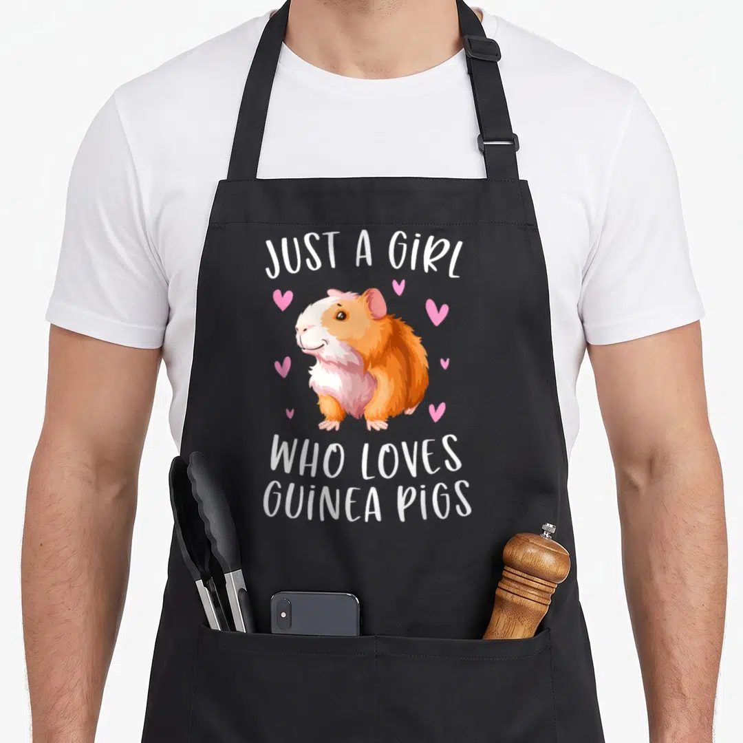 Cavy crazy guinea lady apron - Cartoon guinea pig in orange and white with pink hearts and text — shown on a black cotton canvas apron against a white background
