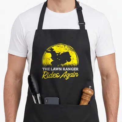 Garden mower apron - Grey rider silhouette on yellow sun with The Lawn Ranger Rides Again text — shown on a black cotton canvas apron against a white background