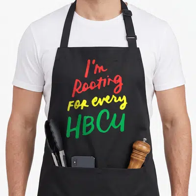 Hbcu university apron - Stacked red yellow green text reading I'm Rooting For Every HBCU — shown on a black cotton canvas apron against a white background