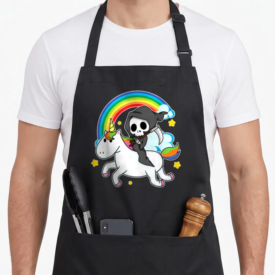 Reaper halloween apron - Cartoon grim reaper riding white unicorn under rainbow with yellow stars and clouds — shown on a black cotton canvas apron against a white background