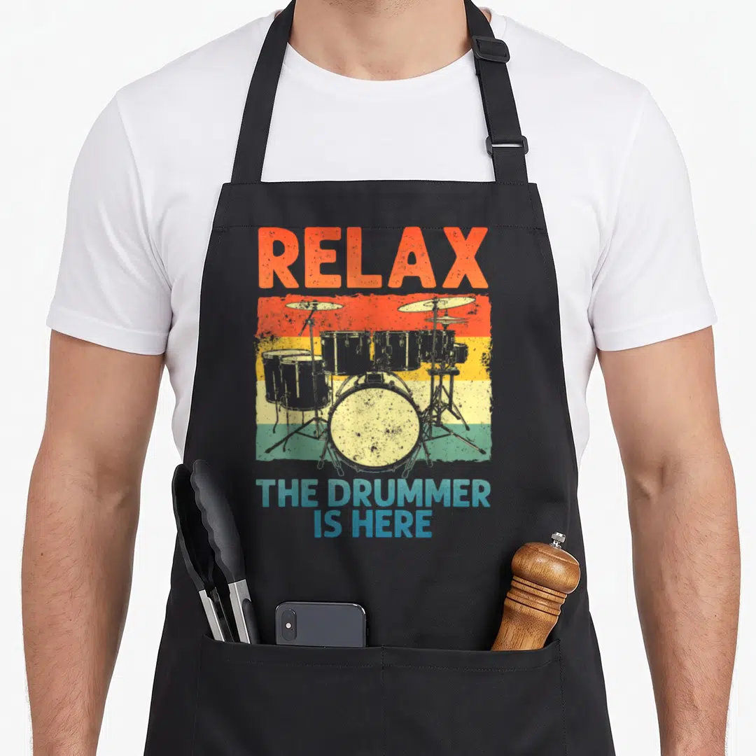 Drumline drum set apron - Relax The Drummer Is Here text over a drum kit on orange yellow green and blue distressed — shown on a black cotton canvas apron against a white background