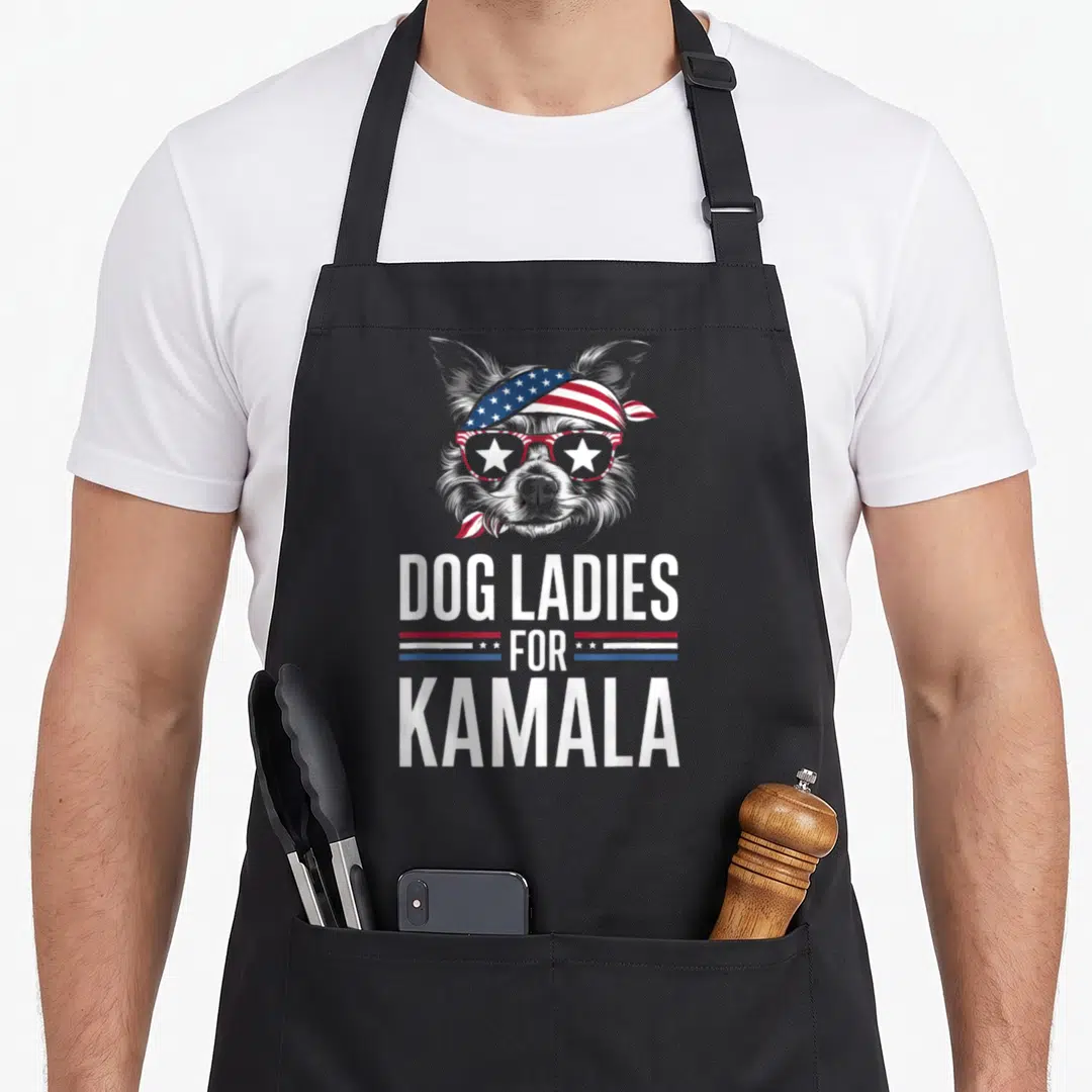 Kamala dog apron - Cartoon grey dog with patriotic bandana and star sunglasses above DOG LADIES FOR KAMALA text — shown on a black cotton canvas apron against a white background