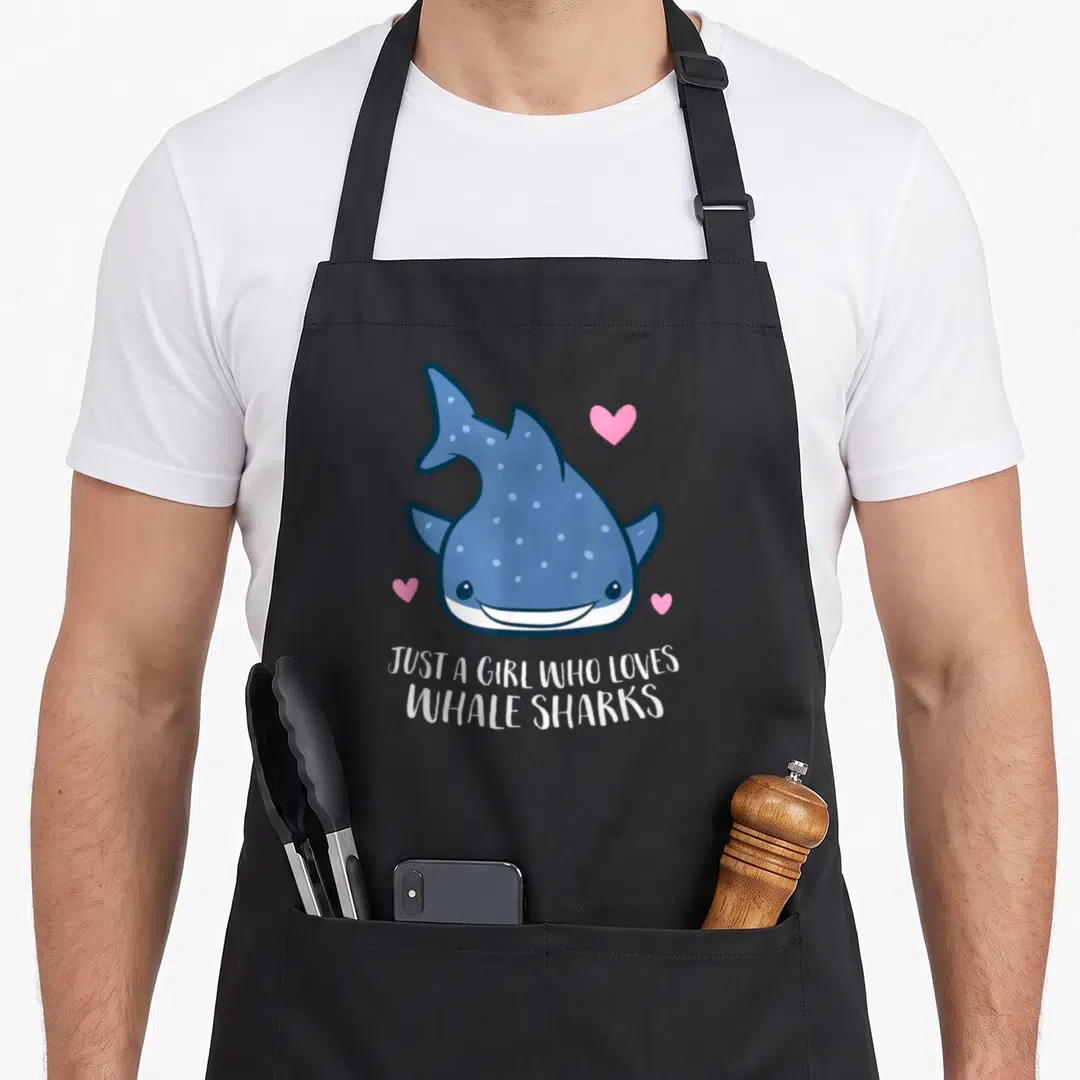 Funny whale shark apron - Cartoon blue whale shark with three pink hearts and white text below — shown on a black cotton canvas apron against a white background