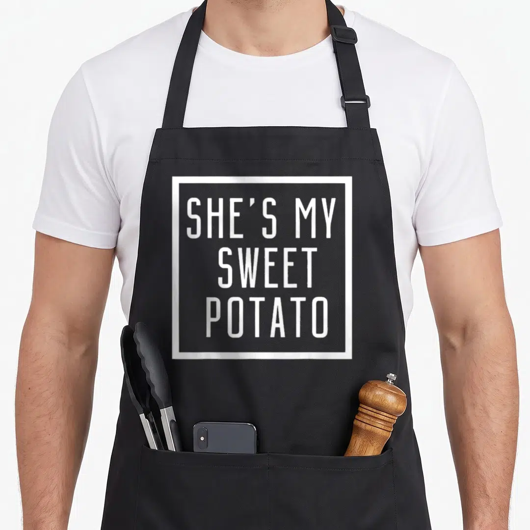 Yam couple potato apron - White text SHE'S MY SWEET POTATO in square border — shown on a black cotton canvas apron against a white background