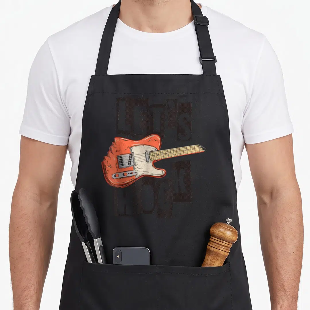 Rock rhythm guitarist apron - Orange electric guitar overlapping distressed LET'S ROCK text on grey dotted blocks — shown on a black cotton canvas apron against a white background