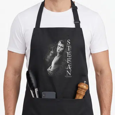 Vampire journal apron - Centered man portrait with vertical white STEFAN text on grey background — shown on a black cotton canvas apron against a white background